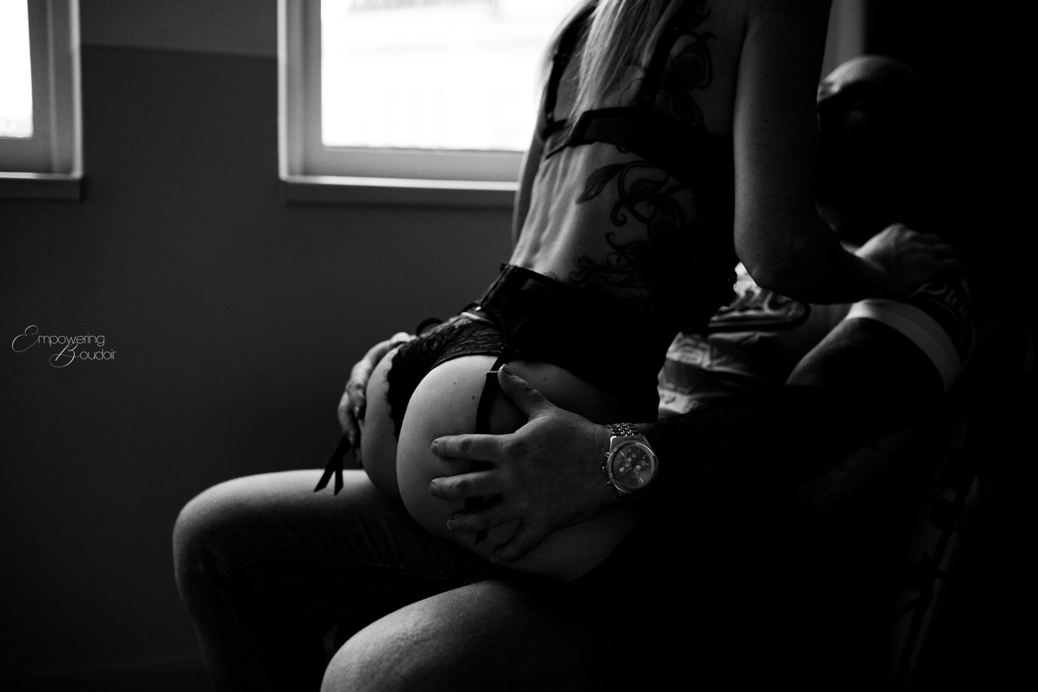 Zwart-witfoto van een vrouw die bij haar partner op schoot zit, bij het raam
