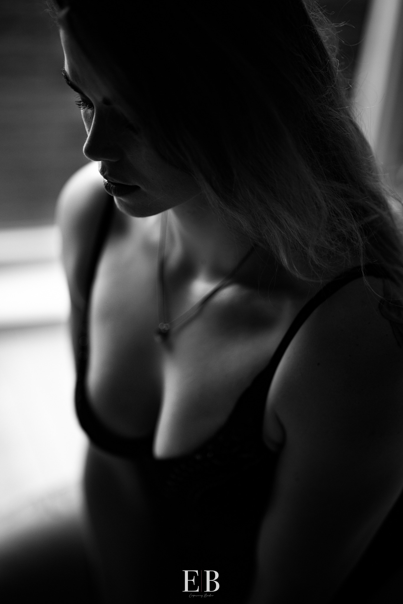 Zwart-witportret van een vrouw met neergeslagen blik in zacht tegenlicht