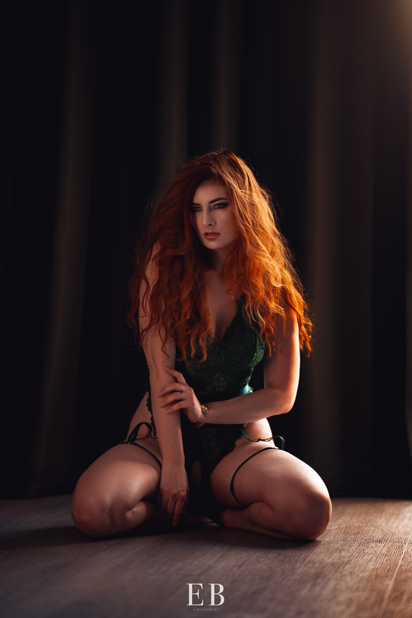 Vrouw met lang rood haar in groene kant, geknield in warm licht